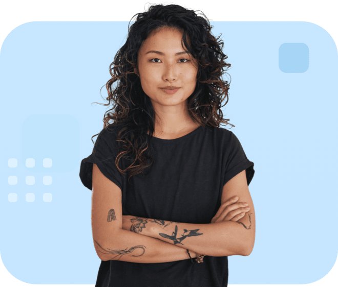 Individual with curly hair, a black top, and standing confidently with crossed arms with tattoos.