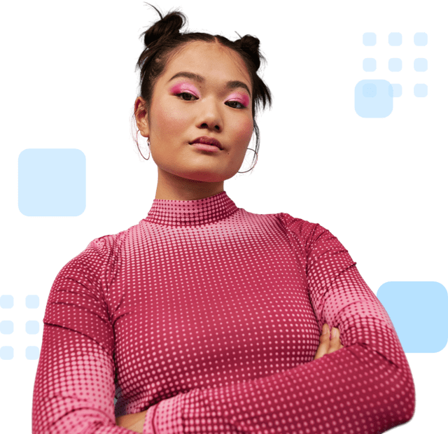 Confident individual with styled hair in space buns, wearing a pink patterned top, and standing with arms crossed.