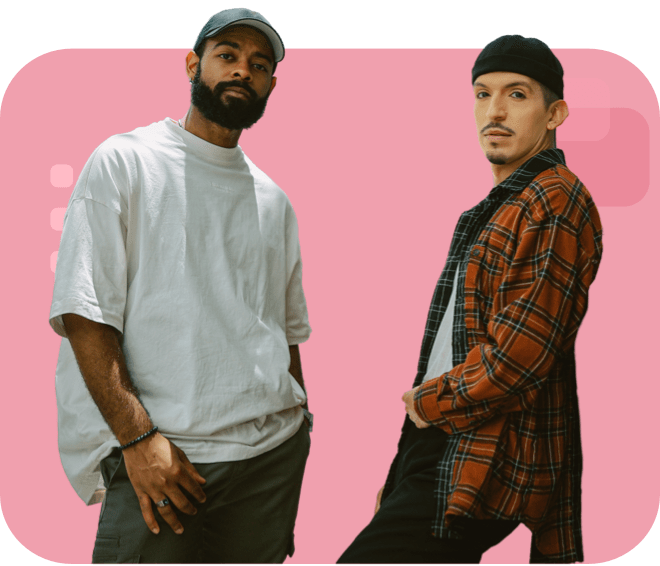 Two confident individuals posing side by side; one wearing a light oversized shirt and cap, the other in a plaid shirt and beanie.