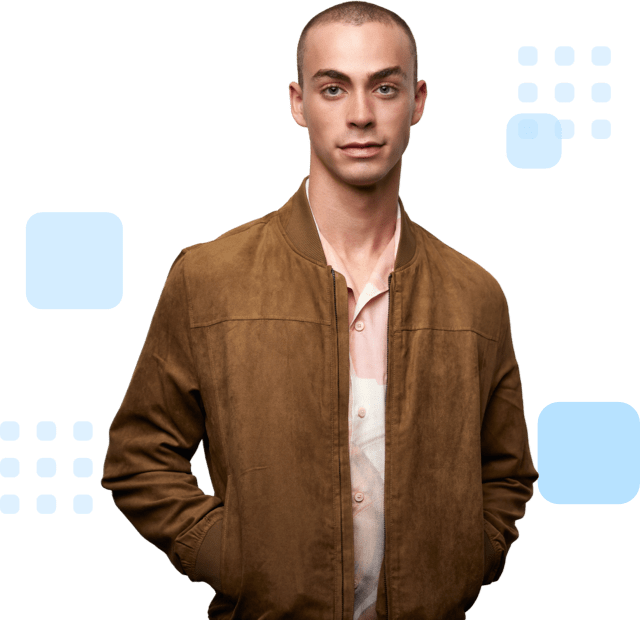 Confident individual with shaved head, wearing a brown jacket over a light shirt, and hands in pockets.